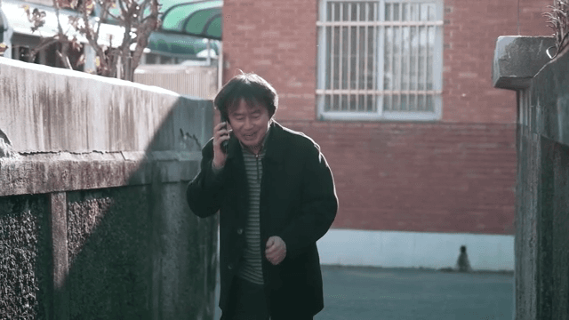 골목에서 전화를 받으며 기뻐하는 남성