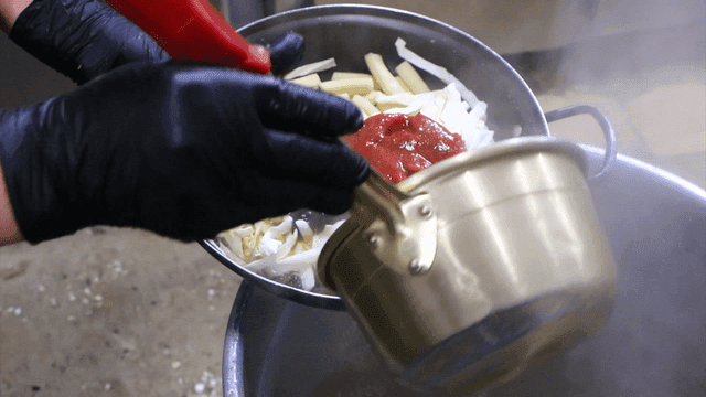 Pouring broth into a pot with tteokbokki ingredients