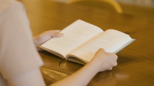 Person Reading a Book at a Wooden Table