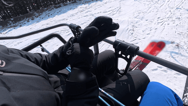 Person wearing gloves on ski lift on snow-covered slope