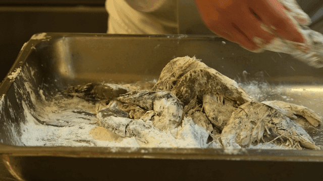 Chef hands-dipping shrimp in flour.