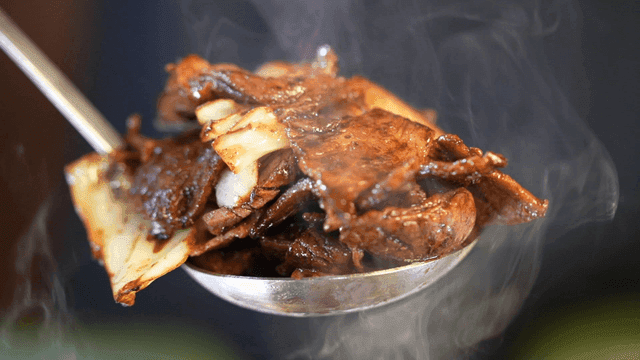 Ladle scooping out steaming hot stir-fried pork