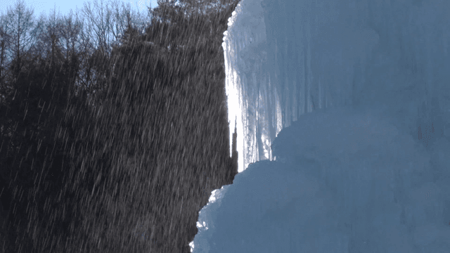 Frozen waterfall bathed in sunlight amidst rain