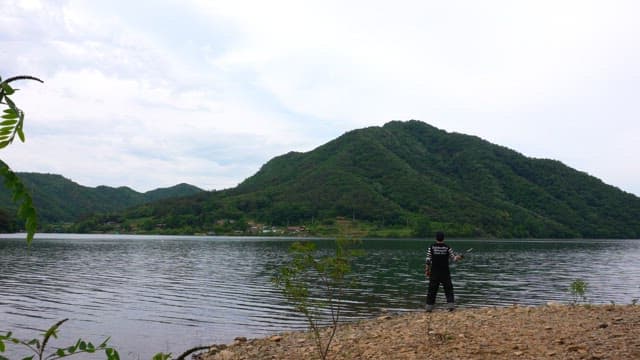 Person fishing by the serene lake on a cloudy day