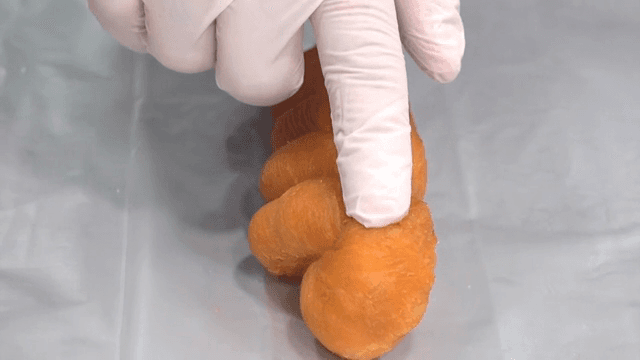 A gloved hand touching a twisted donut