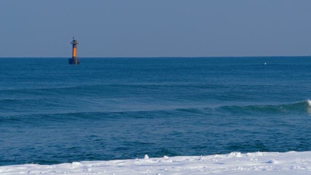 Lone lighthouse stands guard over calm blue ocean waves on a serene winter day