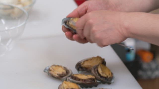 Person shucking fresh abalones on a kitchen counter