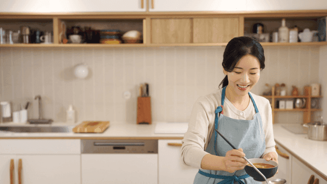 Daughter hugs her mother as she prepares meal in kitchen.