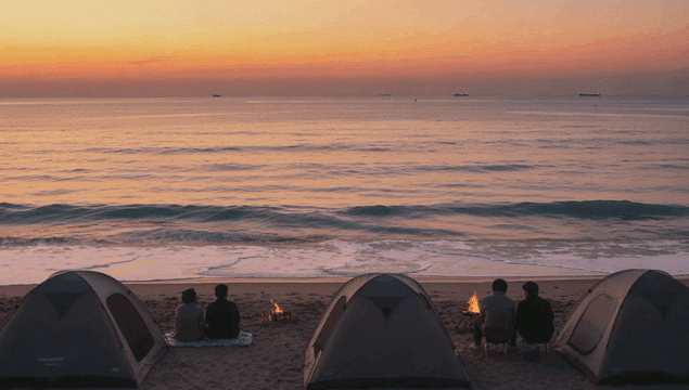 일몰을 보며 모닥불을 피우며 바닷가에서 캠핑하는 사람들