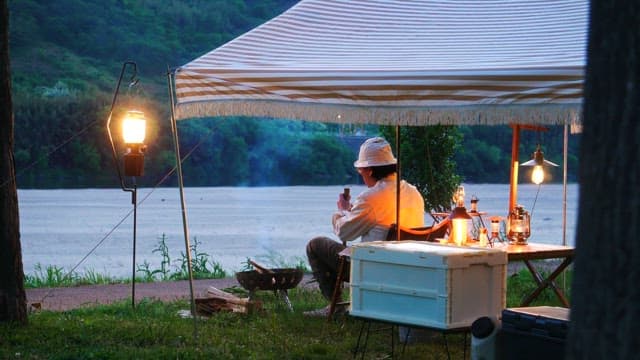 Person relaxing under canopy beside a lake in the evening