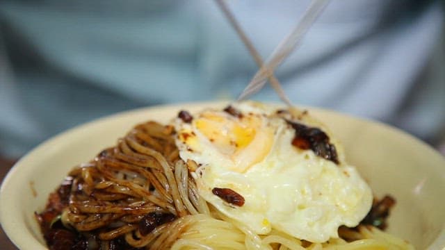 Mixing the noodles with the thick black bean sauce and fried egg using chopsticks