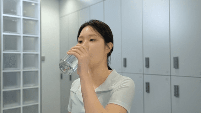 헬스장 라커룸에서 물을 마시는 젊은 여성