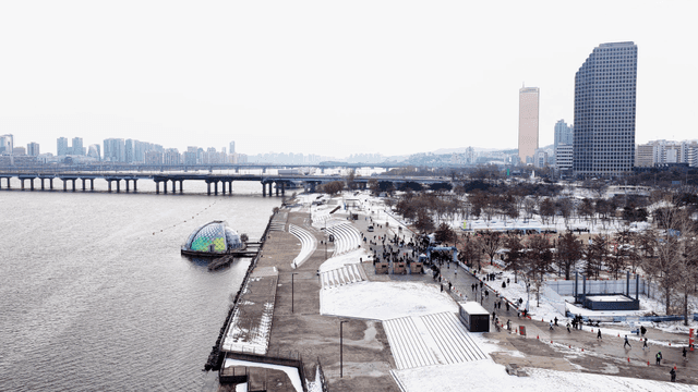 Snow-covered riverside park with city skyline