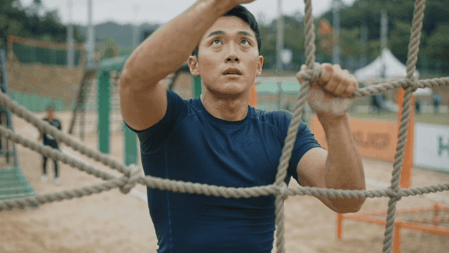 Man climbing a rope in an outdoor obstacle course