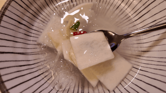 Spoon scooping out dongchimi from white bowl
