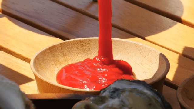 Wooden bowl being filled with red sauce in daylight