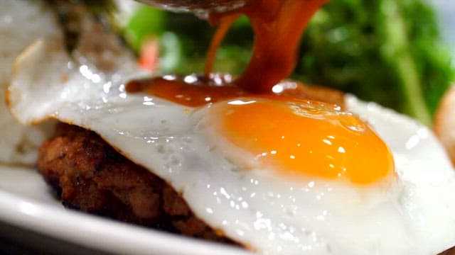 Sauce being poured over hamburger steak with a fried egg