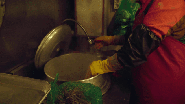 Middle-aged woman washes noodles in hot pot and sink.