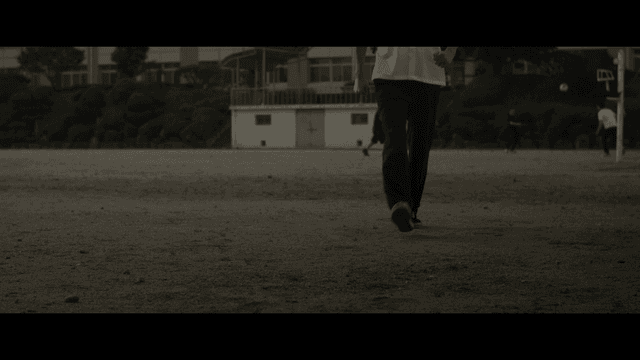 학교 운동장에서 축구 중인 학생들 사이로 걷는 학생