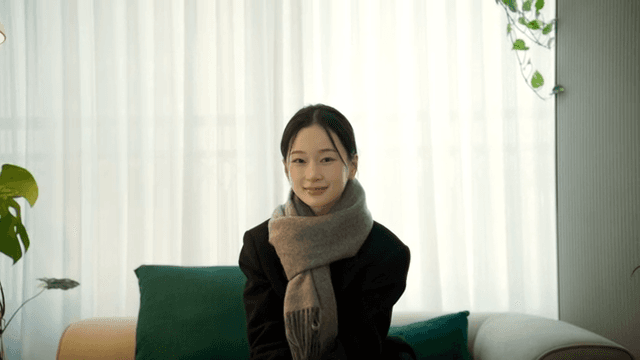 Woman sitting on sofa using her smartphone and smiling while looking straight ahead