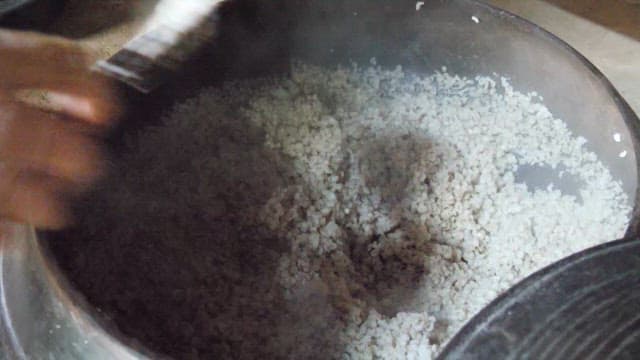 Scooping freshly cooked barley rice from a steaming cauldron