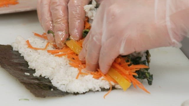 Hands preparing and rolling a kimbap with care