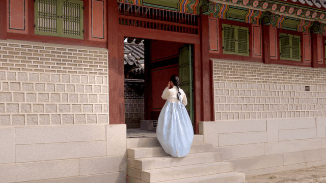 한국 전통 문으로 들어가는 한복을 입은 여성