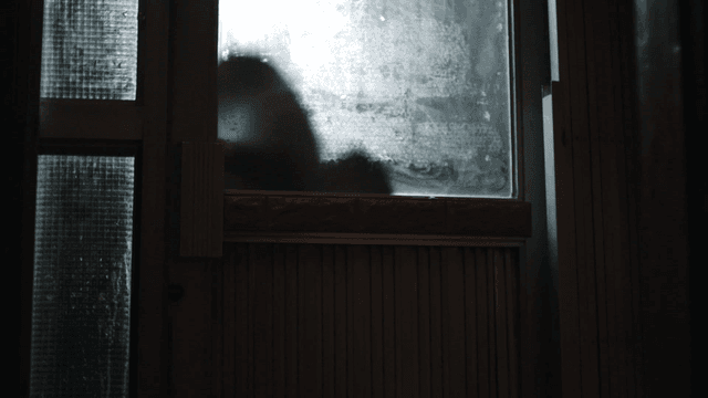 Silhouette of person knocking on door behind opaque glass