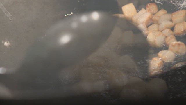 Diced lard being stir-fried in a pan with oil