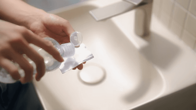 Applying cleansing water to a cotton pad at the bathroom sink