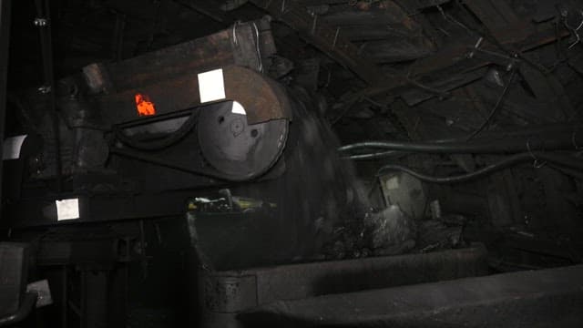 Coal being transported on an industrial conveyor belt in a dimly lit mine