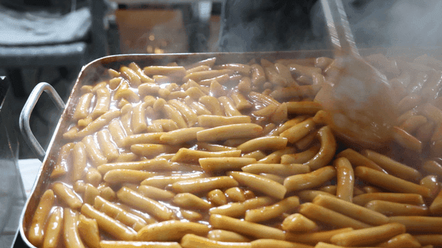 Street vendor stirring tteokbokki in large pan