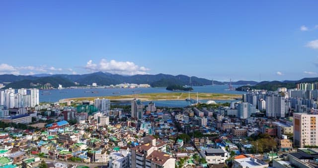 낮부터 밤까지의 하늘 아래 건물과 산, 바다가 있는 도시 경관