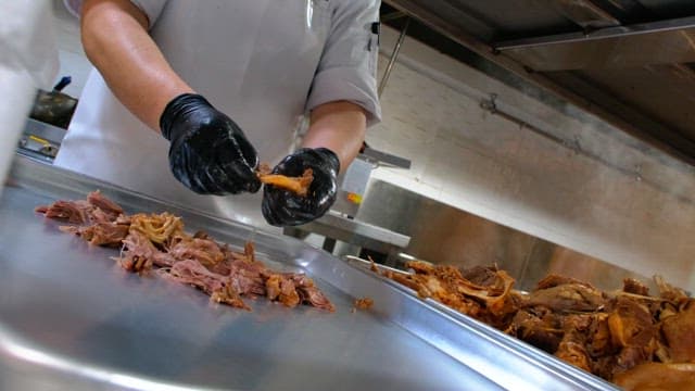 Preparing boiled meat on a metal tray with gloved hands