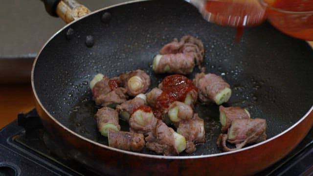 Cooking green onion beef rolls with sauce in a pan