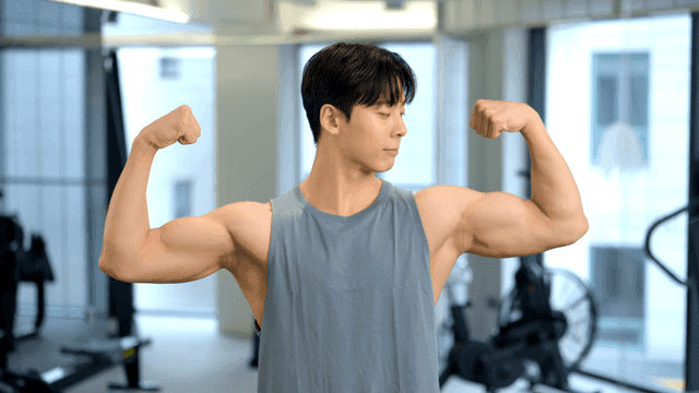 헬스장에서 정면을 보고 양쪽 팔 근육을 자랑하는 젊은 남자