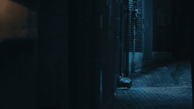 Back of woman walking down dark alley and person following her