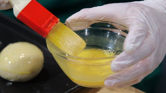 Brushing egg wash on dough balls