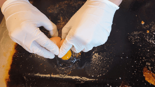 Person breaking egg on hot iron plate