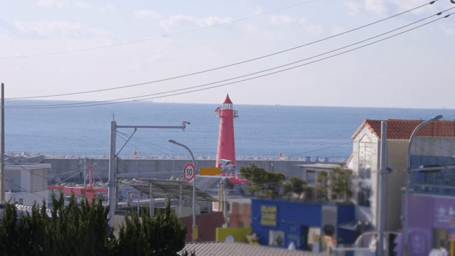 Red lighthouse by the sea with buildings
