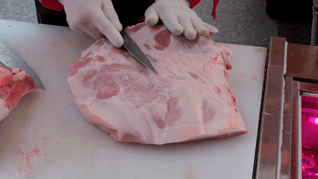 Butcher slicing a large piece of pork
