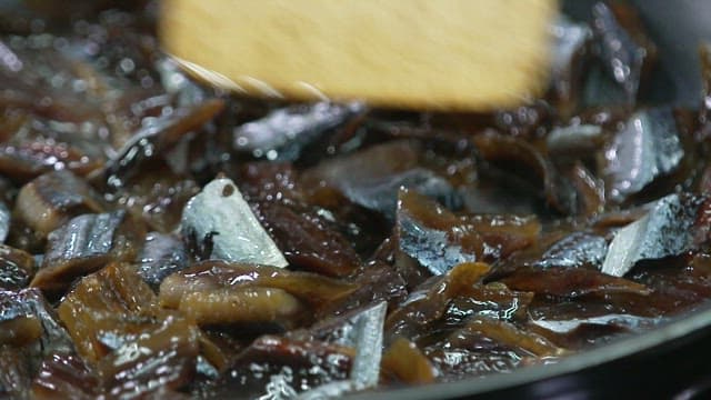 기름을 두른 프라이팬에서 나무 주걱으로 과메기를 볶는 모습