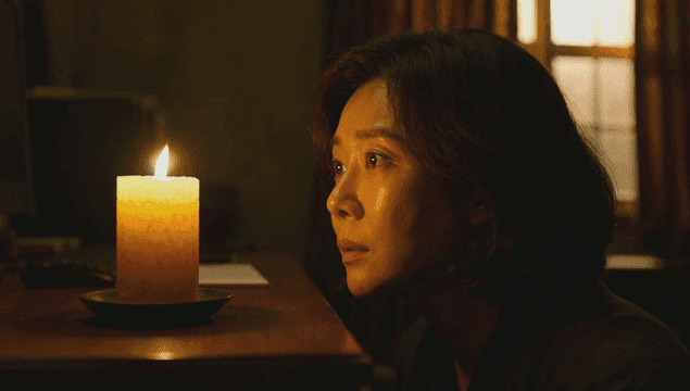 Frightened woman staring at candle in dark room