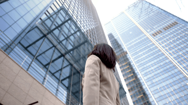 Back view of female office worker looking up at high-rise building