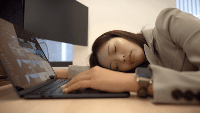 Female office worker asleep leaning against her laptop at her desk