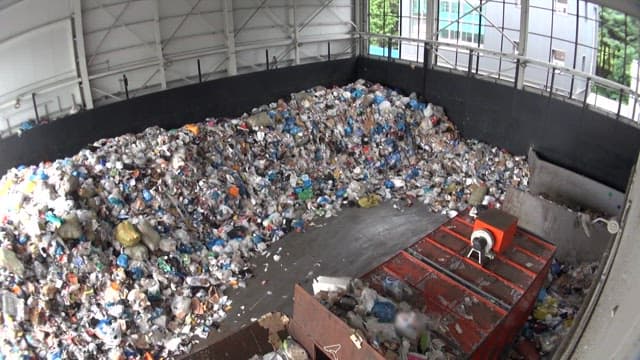 Inside a recycling facility with piles of sorted waste and a yellow bulldozer processing the trash.