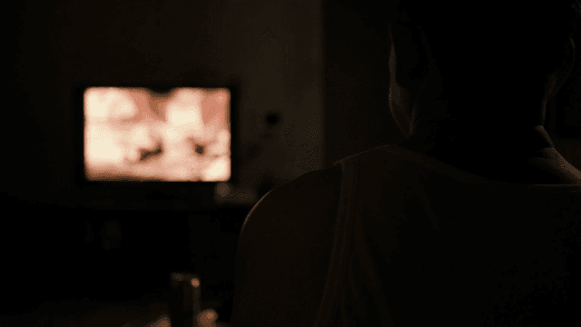 Back view of person watching TV with lights off at night