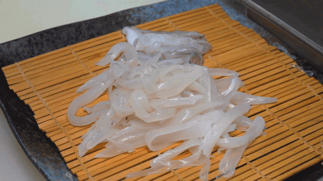 Sliced ​​squid sashimi placed on bamboo mat after being cut on cutting board
