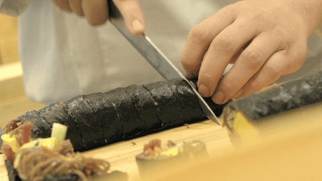 Cutting sushi rolls on wooden cutting board