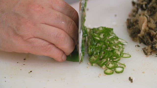 Slicing fresh green chili peppers on a cutting board